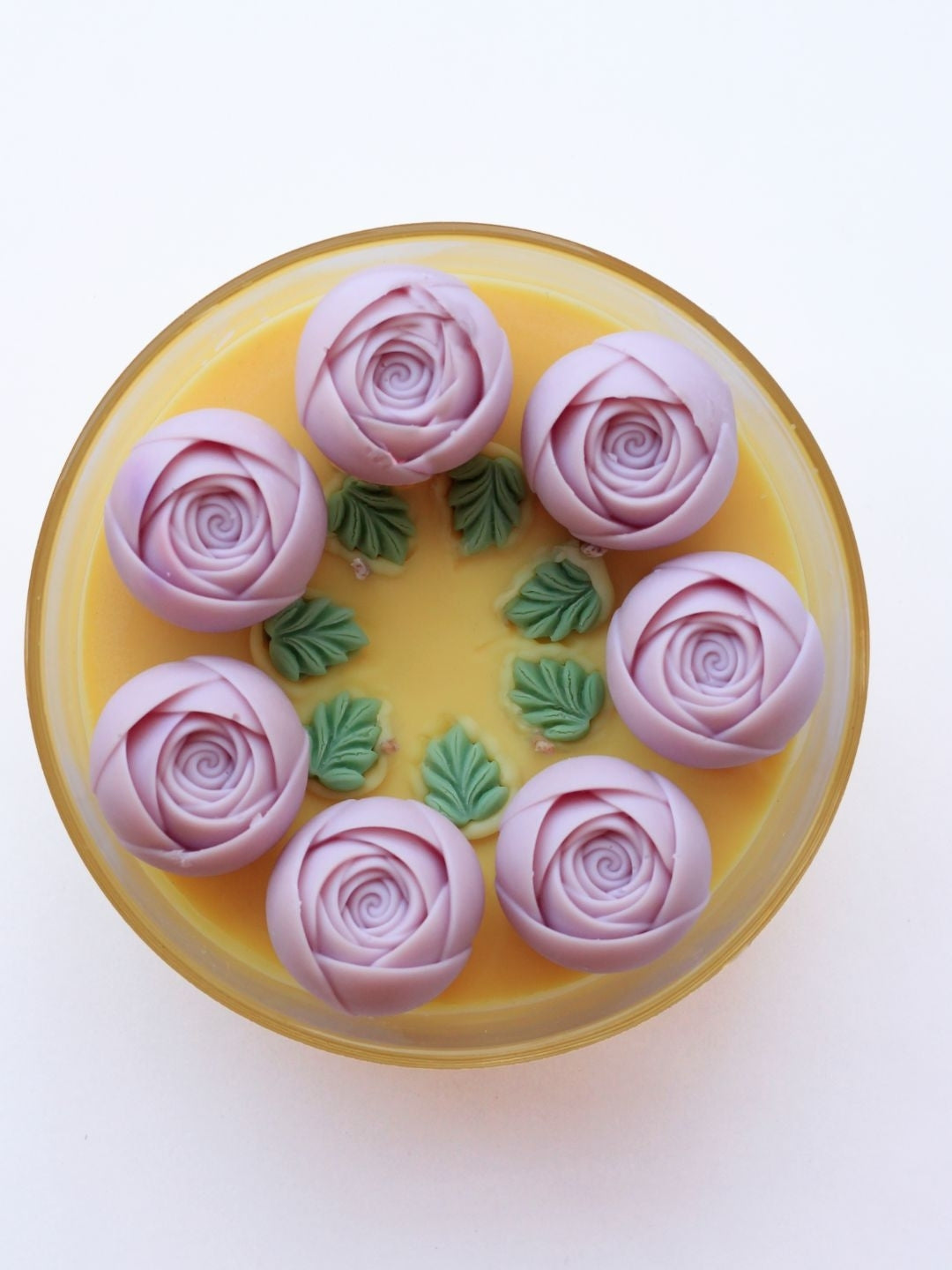 The image shows a candle jar of 5.5 inch diameter, with 7 roses and leaves on yellow coconut wax. it is clear it has 4 wicks.