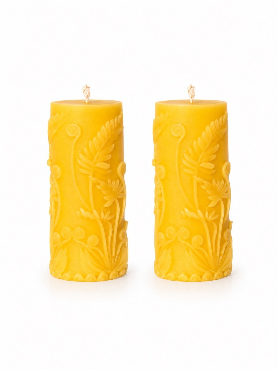 A pair of yellow pillar candles with embossed floral and leaf patterns, standing upright on a white background.