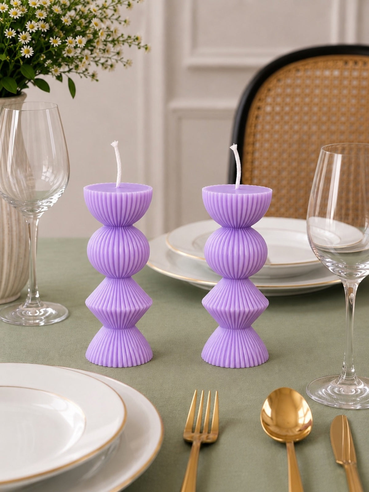 Two lavender ribbed pillar candles styled on a dining table with white plates, gold cutlery, wine glasses, and a woven chair in the background. Velvetine Soirée Beeswax Candle Pillar Candles