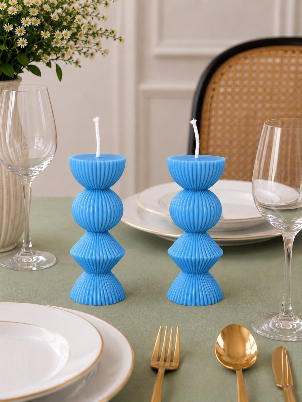 Two bright blue ribbed pillar candles with white wicks, styled on a green tablecloth with white plates, gold cutlery, wine glasses, and a floral arrangement in the background. Velvetine Soirée Beeswax Candle Pillar Candles
